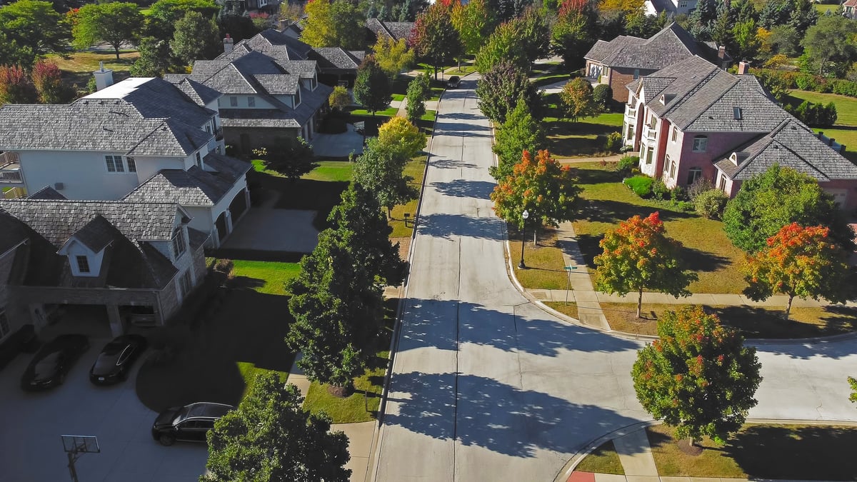A tidy, well-maintained residential street with tree-lined sidewalks in warm light
